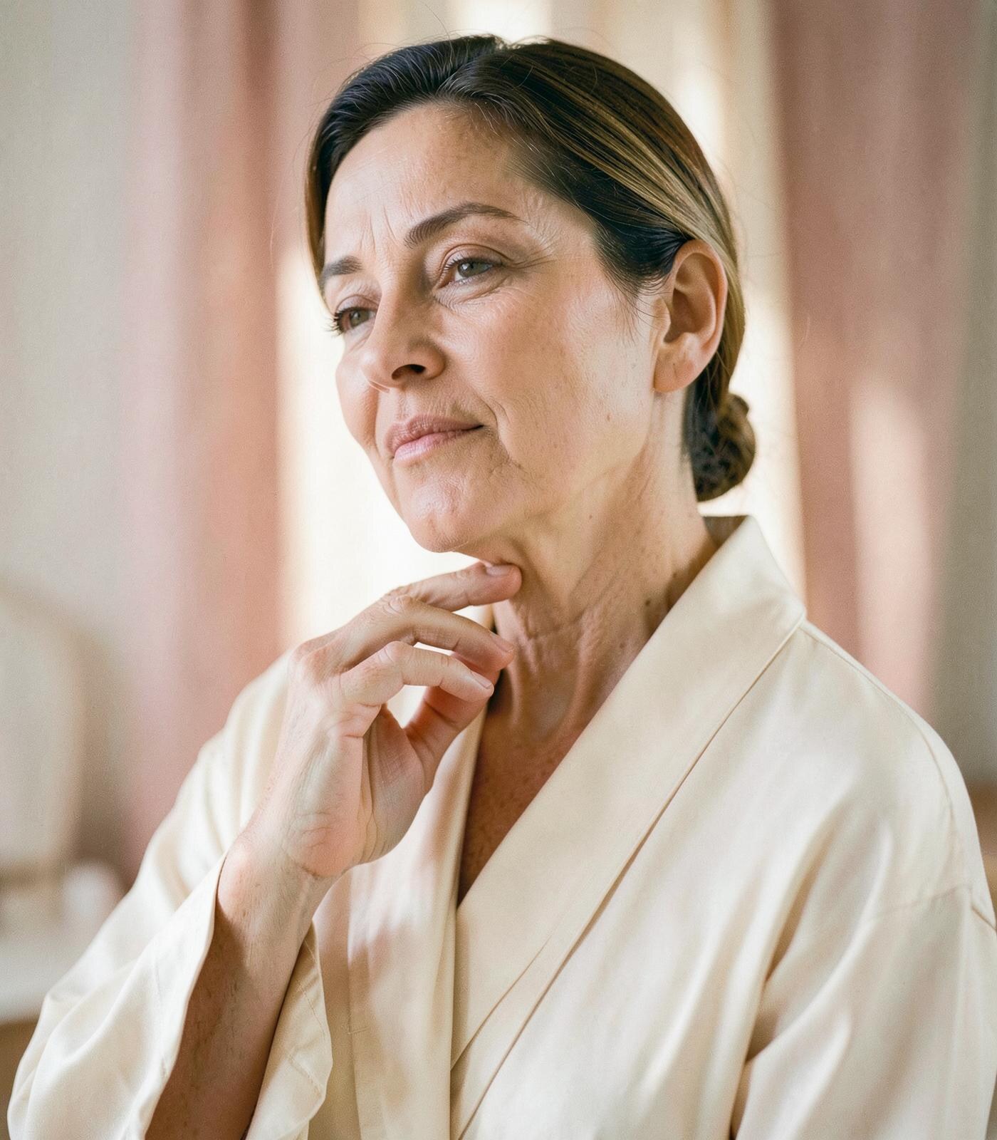A woman in a silk robe touching the base of her neck in morning light